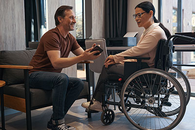 Disabled woman in a wheelchair talking to her co-worker in her office