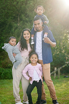 Mom and dad posing for a photo with their three young children in the backyard