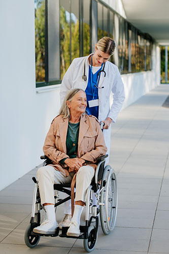 Senior woman in a wheelchair being pushed by a nurse in an assisted living facility