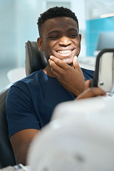 Man in the dentist's chair looking at his clean white teeth and smiling