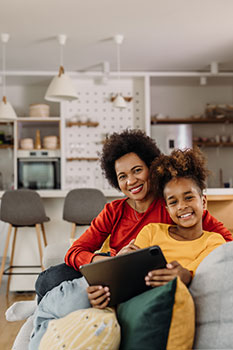 Woman and her daughter sitting on the couch using a tablet to look up whole life insurance quotes