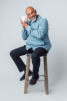 Retired man smiling and holding up a piggy bank, representing the guaranteed income stream annuities provide