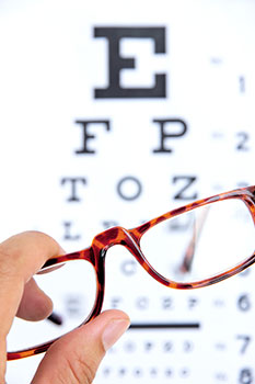 Close-up of a hand holding a pair of glasses over an eye chart